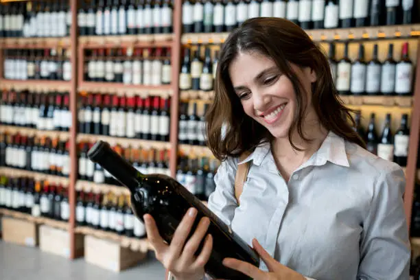 Beautiful female client at a wine store looking at a winebottle to purchase very happy and smiling