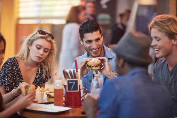 istock Man with burger sitting by friends in restaurant 924150146