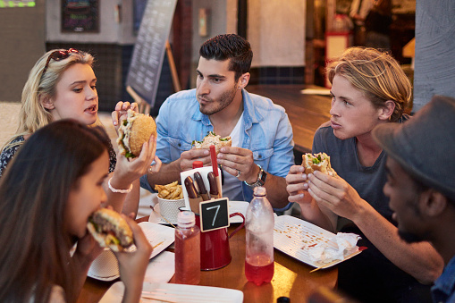 Young male and female friends having burgers in restaurant. Tourists are communicating while eating. Men and women are spending time together.