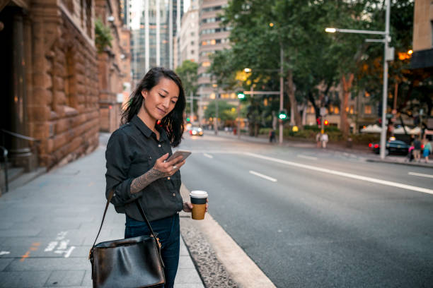 Young businesswoman waiting for taxi in Sydney Young businesswoman waiting for taxi in Sydney. She has a coffee to go. text messaging photos stock pictures, royalty-free photos & images