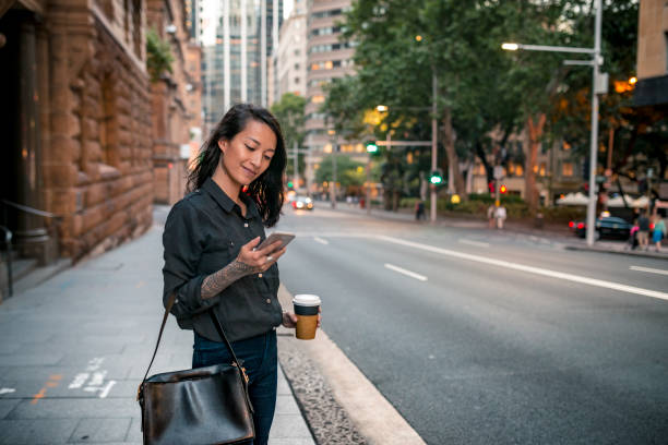 Young businesswoman waiting for taxi in Sydney Young businesswoman waiting for taxi in Sydney. She has a coffee to go. happy car asian stock pictures, royalty-free photos & images