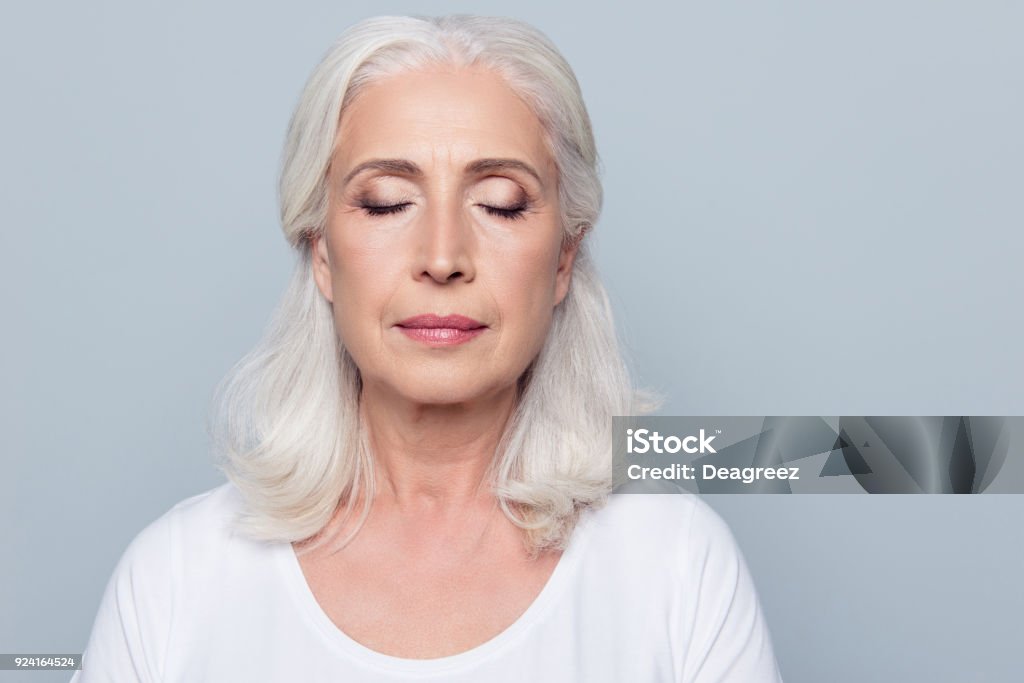 Close up portrait of confident concentrated mature woman with wrinkles on face, with closed eyes, with nude make up, isolated on gray background Eyelid Stock Photo