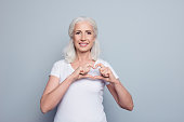 Perfect, nice, aged, old, pretty woman, lover in t-shirt making, showing heart figure with fingers, looking at camera, celebrating woman's day, standing over gray background