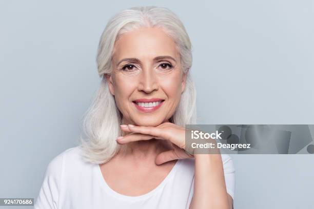 Charming Old Woman Holding Hand Under Chin With Beaming Smile Looking At Camera Over Gray Background Stock Photo - Download Image Now