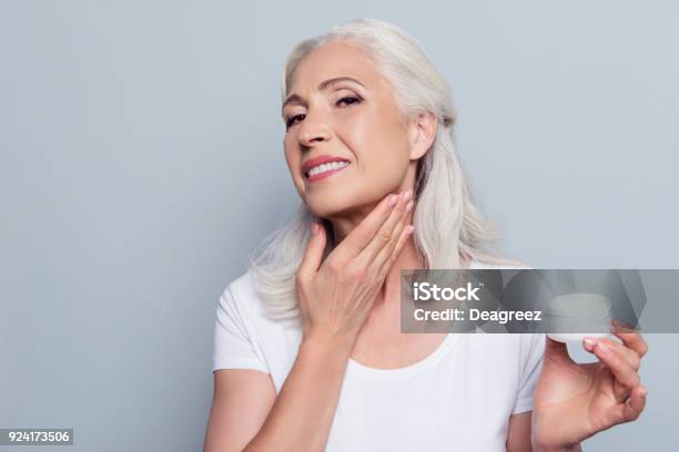 Mature Adult Senior Woman With Gray Hair Is Taking Care About Her Face And Neck She Is Smearing Natural Night Cream Using Hand Before Going To Bed Isolated On Gray Background Stock Photo - Download Image Now