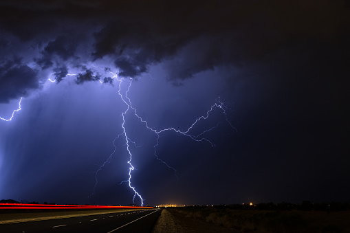 Lightning strikes during a nighttime thunderstorm as cars pass on a nearby highway.