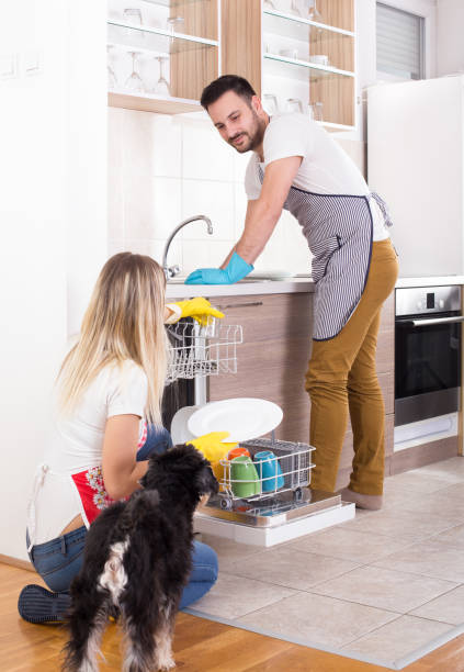 Young couple unloading dishwasher Young happy couple unloading dishwasher with clean crockery. Working together and helping each other in housework dog dishwasher stock pictures, royalty-free photos & images