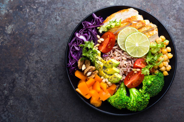 istock Buddha bowl dish with chicken fillet, brown rice, avocado, pepper, tomato, broccoli, red cabbage, chickpea, fresh lettuce salad, pine nuts and walnuts. Healthy balanced eating. Top view 924194436