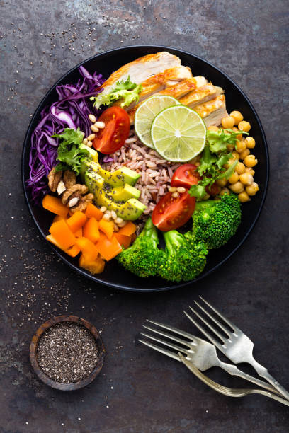 istock Buddha bowl dish with chicken fillet, brown rice, avocado, pepper, tomato, broccoli, red cabbage, chickpea, fresh lettuce salad, pine nuts and walnuts. Healthy balanced eating. Top view 924194478