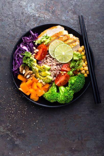 istock Buddha bowl dish with chicken fillet, brown rice, avocado, pepper, tomato, broccoli, red cabbage, chickpea, fresh lettuce salad, pine nuts and walnuts. Healthy balanced eating. Top view 924194490