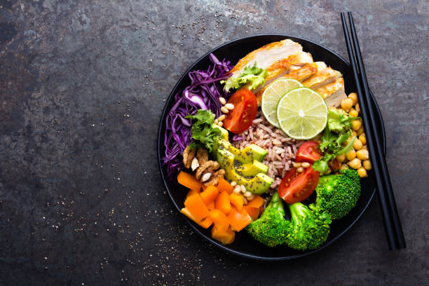 istock Buddha bowl dish with chicken fillet, brown rice, avocado, pepper, tomato, broccoli, red cabbage, chickpea, fresh lettuce salad, pine nuts and walnuts. Healthy balanced eating. Top view 924194524