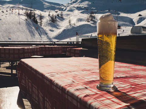 Large draft beer on a table with a red and white checked pattern cloth. Winter landscape in background with ski slope. Vintage style.