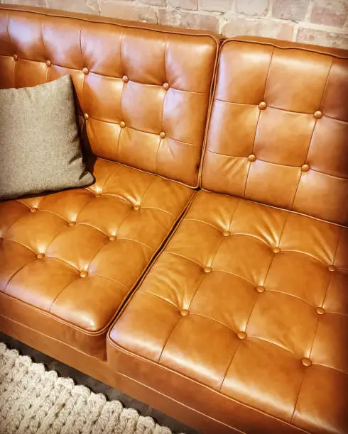 Luxurious brown leather sofa with cushion, on a knitted rug.