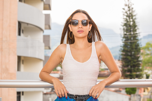 Young lady in her twenties pose for a portrait. She is latin. She is wearing a tank top and sunglasses.