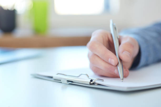 istock Male hand holding silver pen ready to make note in a clipboard. Businessman or employee at workplace writing business ideas, plans or tasks. Office life or education concept. 924257890