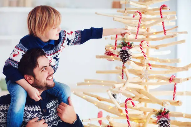 Photo of happy family, father and son decorate handcrafted christmas tree made of driftwood at home