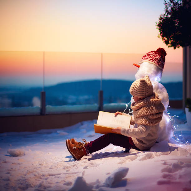 fiaba invernale. ragazzo, ragazzo che legge libro interessante per il suo amico pupazzo di neve nel cortile di casa - garment snow little boys child foto e immagini stock