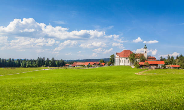 Beautiful view of famous oval rococo Pilgrimage Church of Wies (Wieskirche), a UNESCO World Heritage Site since 1983, with green meadows on a sunny day with blue sky and clouds in Bavaria, Germany