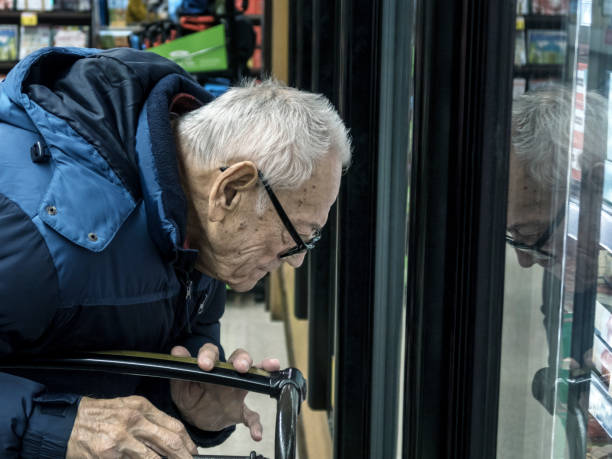 shopper di alimentari anziano riflesso nella finestra del refrigeratore della sezione refrigerata - senior adult aging process supermarket shopping foto e immagini stock