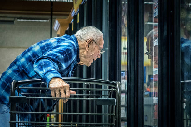 anziano supermercato alimentari shopper guardando attraverso la sezione refrigerata finestra più fresca - senior adult aging process supermarket shopping foto e immagini stock