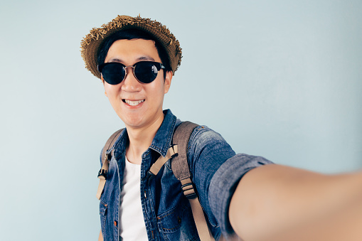 Young Asian tourist smiling and taking a selfie isolated over pastel blue background