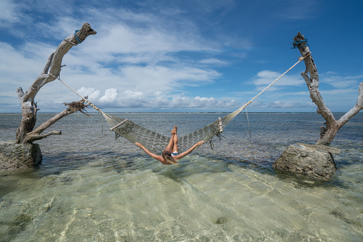 View of a young woman relaxing on hammock over the water, people travel vacations concept. Shot in the Gili Islands, Lombok, Indonesia