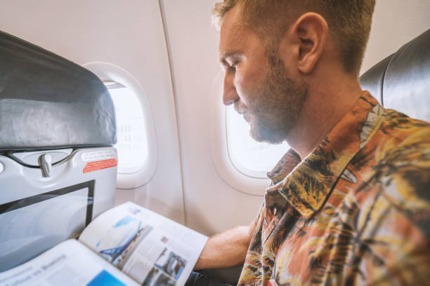 istock Young man in airplane reading magazine 924329560