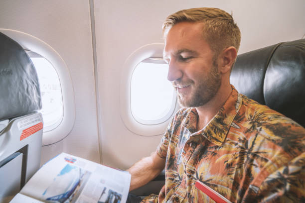 istock Young man in airplane reading magazine 924329680