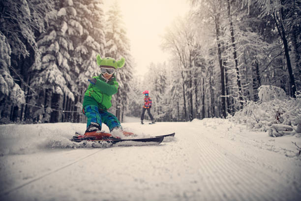 Little boy skiing skillfully on a beautiful winter day.  Ski slope in a winter forest. Sister visible in the background. The boy is focused on making a dynamic turn.\n