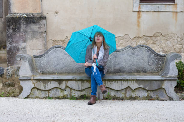 Sicily: Rainy Day in a City Park in Ragusa Ibla; Woman Sis on Antique Bench with Turquoise Umbrella. Shot in Ragusa Ibla, Sicily, Italy.