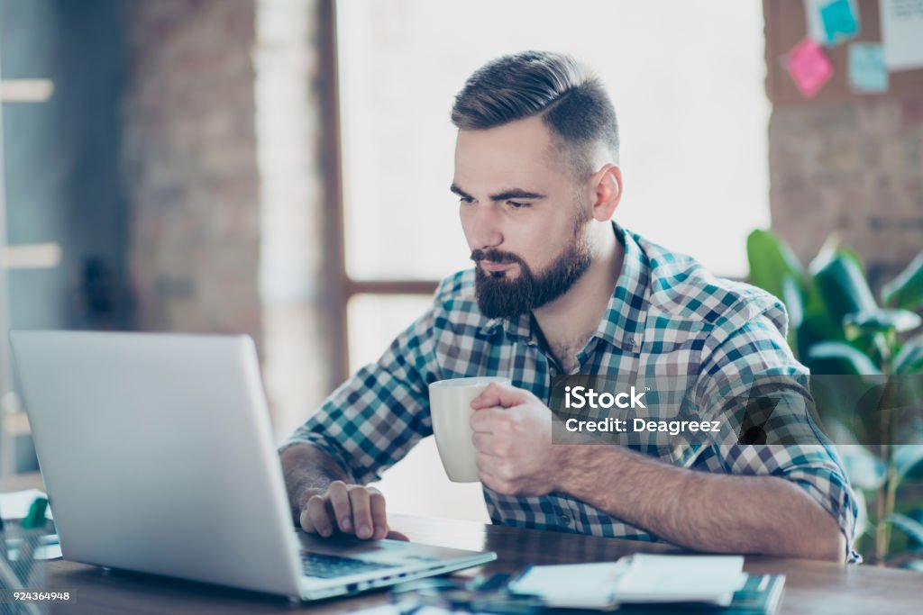 Concept of having a break at work. Concentrated calm peaceful serious office worker  watching carefully a video on the internet using his laptop and drinking tea Men Stock Photo