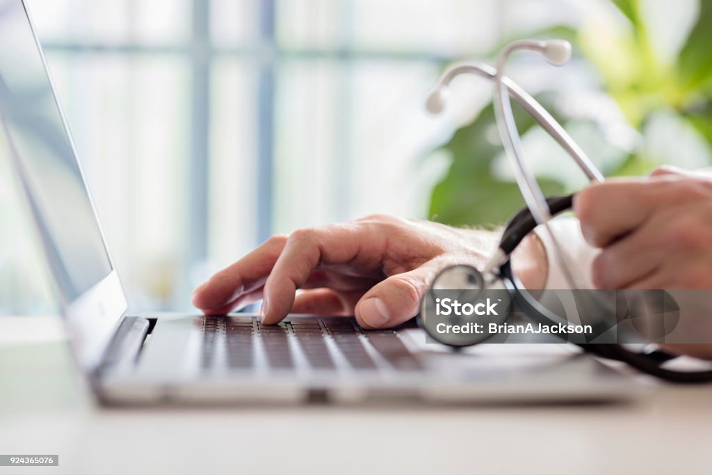 Doctor entering patient notes on laptop in surgery Doctor entering patient notes on a laptop in surgery Doctor Stock Photo