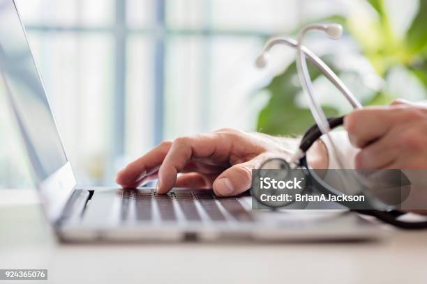 Doctor Entering Patient Notes On Laptop In Surgery Stock Photo - Download Image Now - Doctor, Healthcare And Medicine, General Practitioner