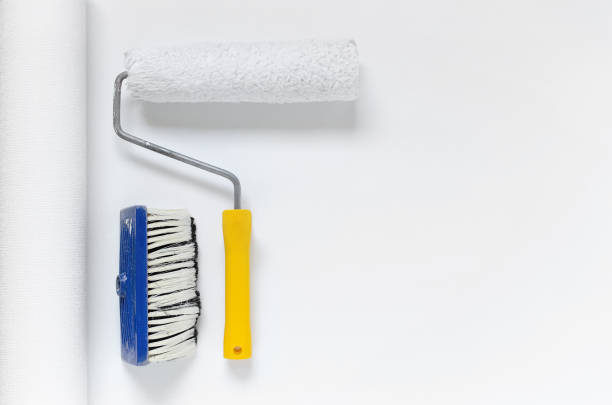 tools for wallpapering, paint roller and a brush on white wallpaper roll
