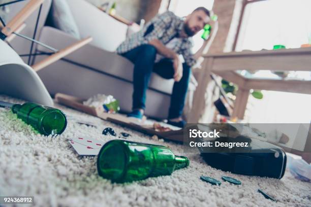 Concept Of Having Headache After Global Party Close Up Lowangle Photo Of Empty Green Transparent Beer Bottles Lying On Nappy Beige Carpet Guy With Nausea Sitting On Sofa In Ob Blurred Background Stock Photo - Download Image Now