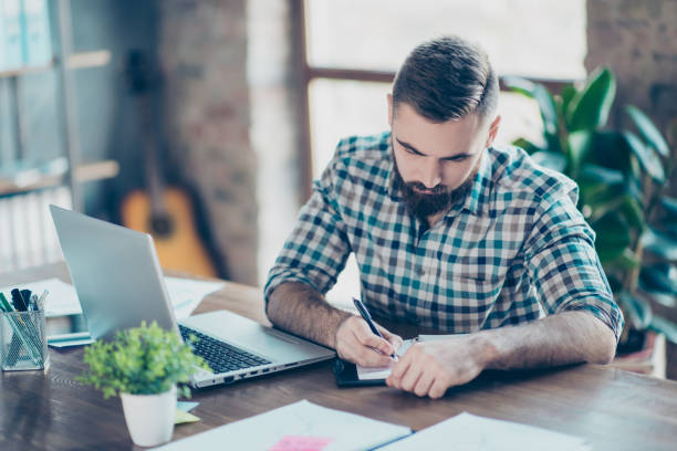 atento inteligente inteligente inteligente estudante do sexo masculino com camisa quadriculada é fazendo lição de casa em casa na frente do computador moderno - male education college student nerd - fotografias e filmes do acervo