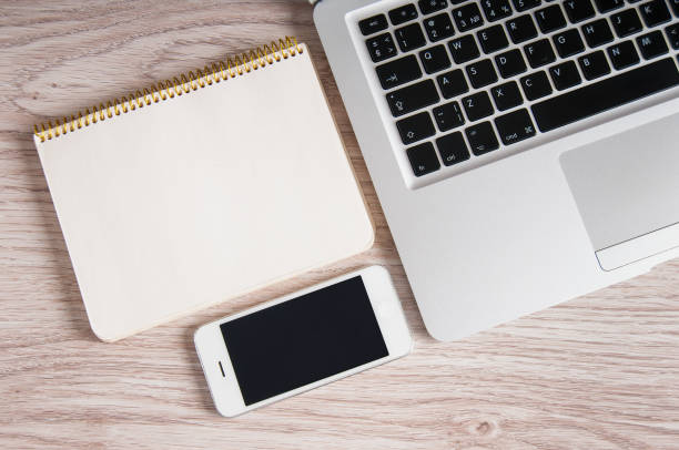 Notepad, laptop, mobile phone on white wood table