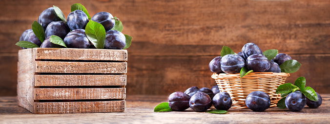 fresh plums with leaves in a wooden box on a wooden table