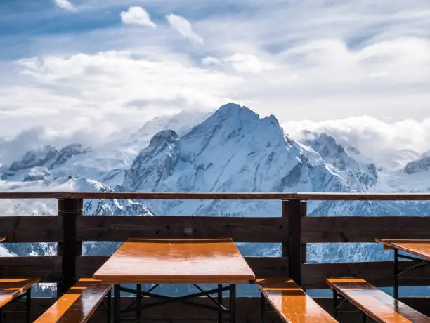 View of snowy mountains from restaurant in the alps. Lunch break from skiing in the sun. Empty tables and seats in foreground.