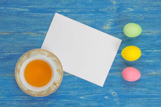 colorful eggs, tea cup and empty paper sheet on blue table