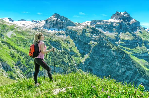girl traveler with sticks for a walk, against a backdrop of mountain peaks, admires the nature and mountain landscapes of Switzerland, the Engelberg resort