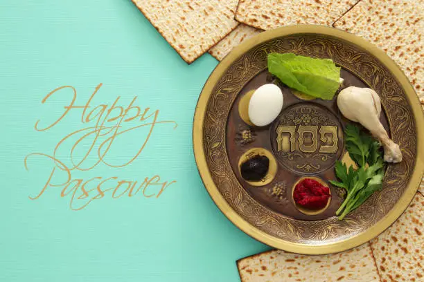 Pesah celebration concept (jewish Passover holiday). Traditional pesah plate with five symbols: horseradish, celery, egg, bone, maror, charoset. Text in hebrew: Passover
