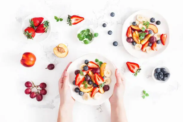 Photo of Woman holding fruit salad. Flat lay, top view
