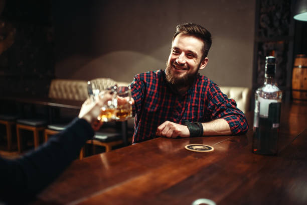 Two men clink glasses at a bar, friends drink strong alcohol and having fun. Happy leisure in pub