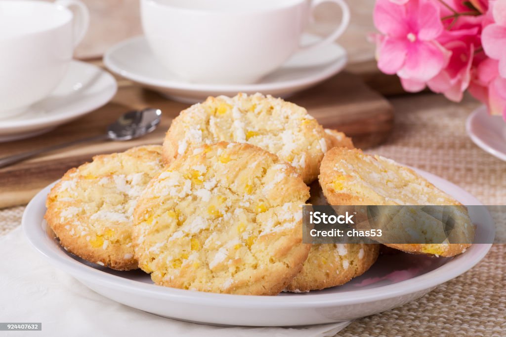 Lemon Cookies Pile of lemon cookies on a plate with two coffee cups and flowers in background Lemon Cookie Stock Photo