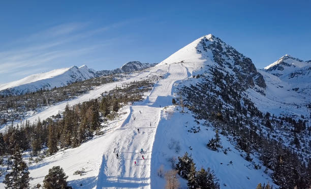 Aerial view of skiers on ski slope on Strbske Pleso resort in High Tatras mountains, Slovakia. Skiers on ski slope in High Tatras mountains aerial. pleso stock pictures, royalty-free photos & images