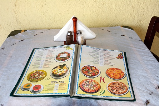 Pizza and salad menu displayed on a dining table at the Greek Taverna Valentino edge of the beach, Bali, Crete, Greece, Europe.