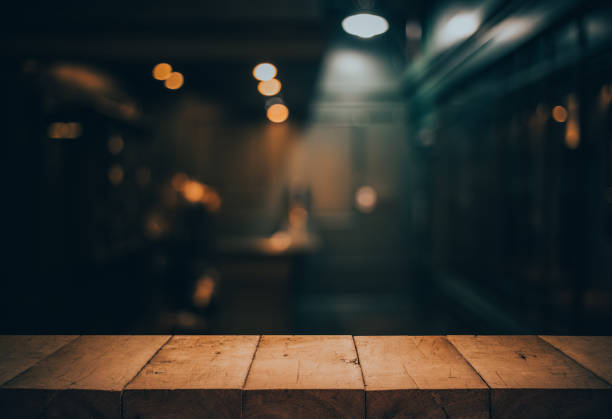 Wood table top on blurred of counter cafe shop with light bulb.Background for montage product display or design key visual Wood table top on blurred of counter cafe shop with light bulb.Background for montage product display or design key visual layout. restaurant table stock pictures, royalty-free photos & images