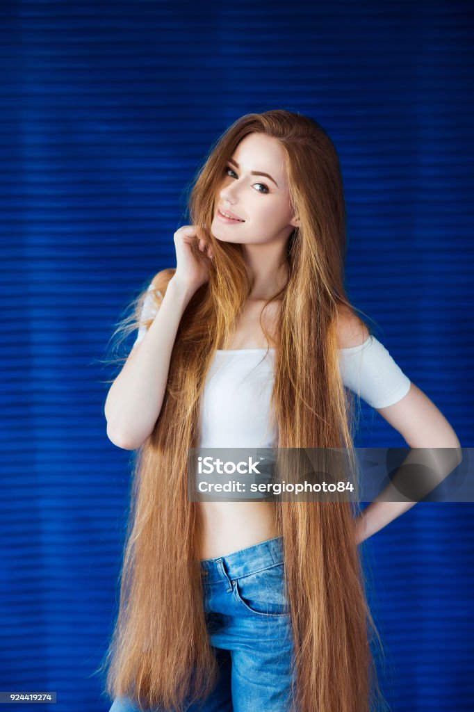 Young Beautiful Woman In A White Shirt And Jeans With Very Long Natural Hair  Near A Blue Wall In Loft Interior Stock Photo - Download Image Now - iStock