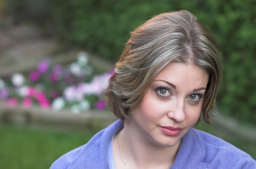 Caucasian woman in her late 20's looks up at you, with a flowery garden background